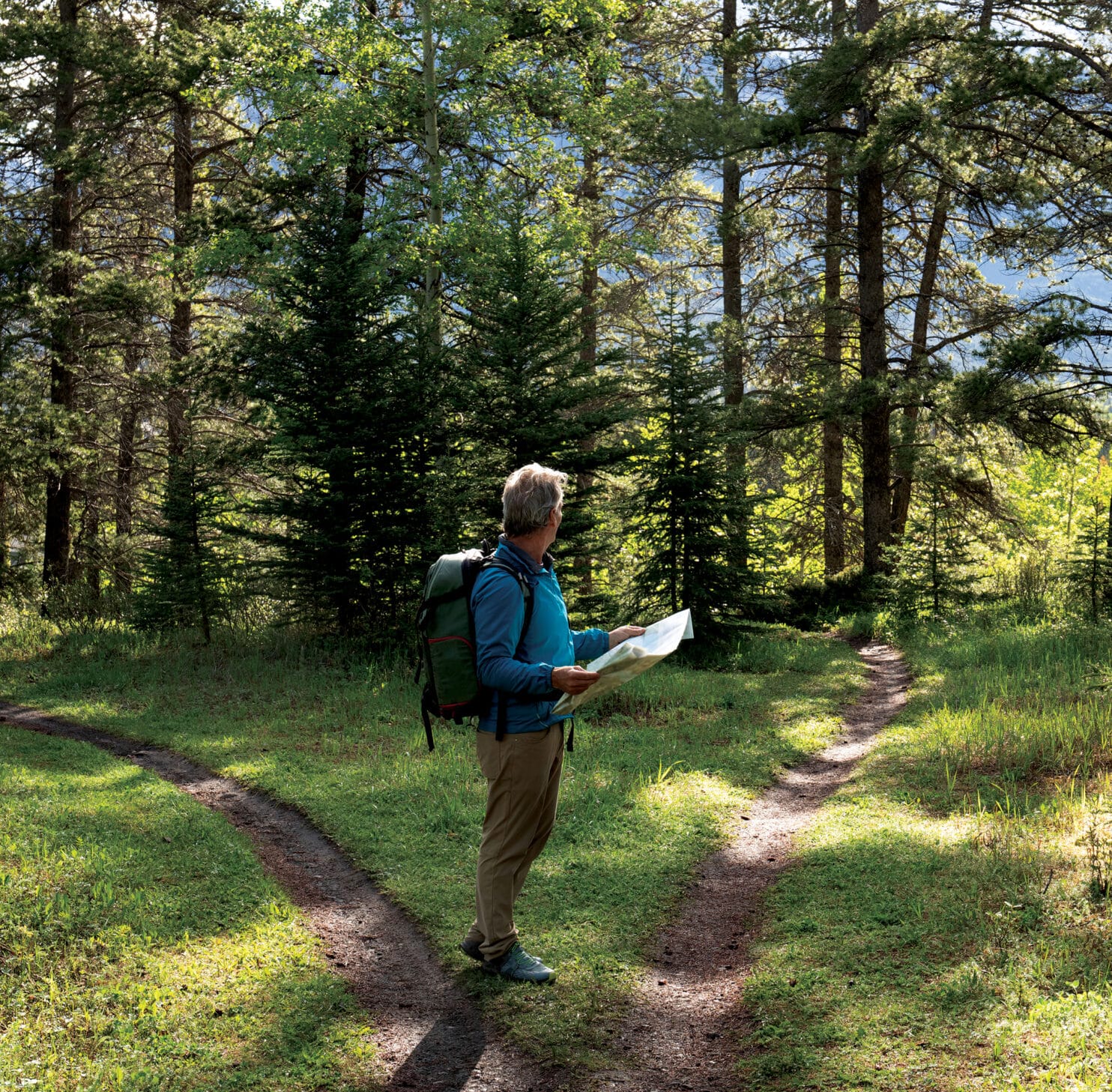 Man hiking in forest looking at map deciding which path to take